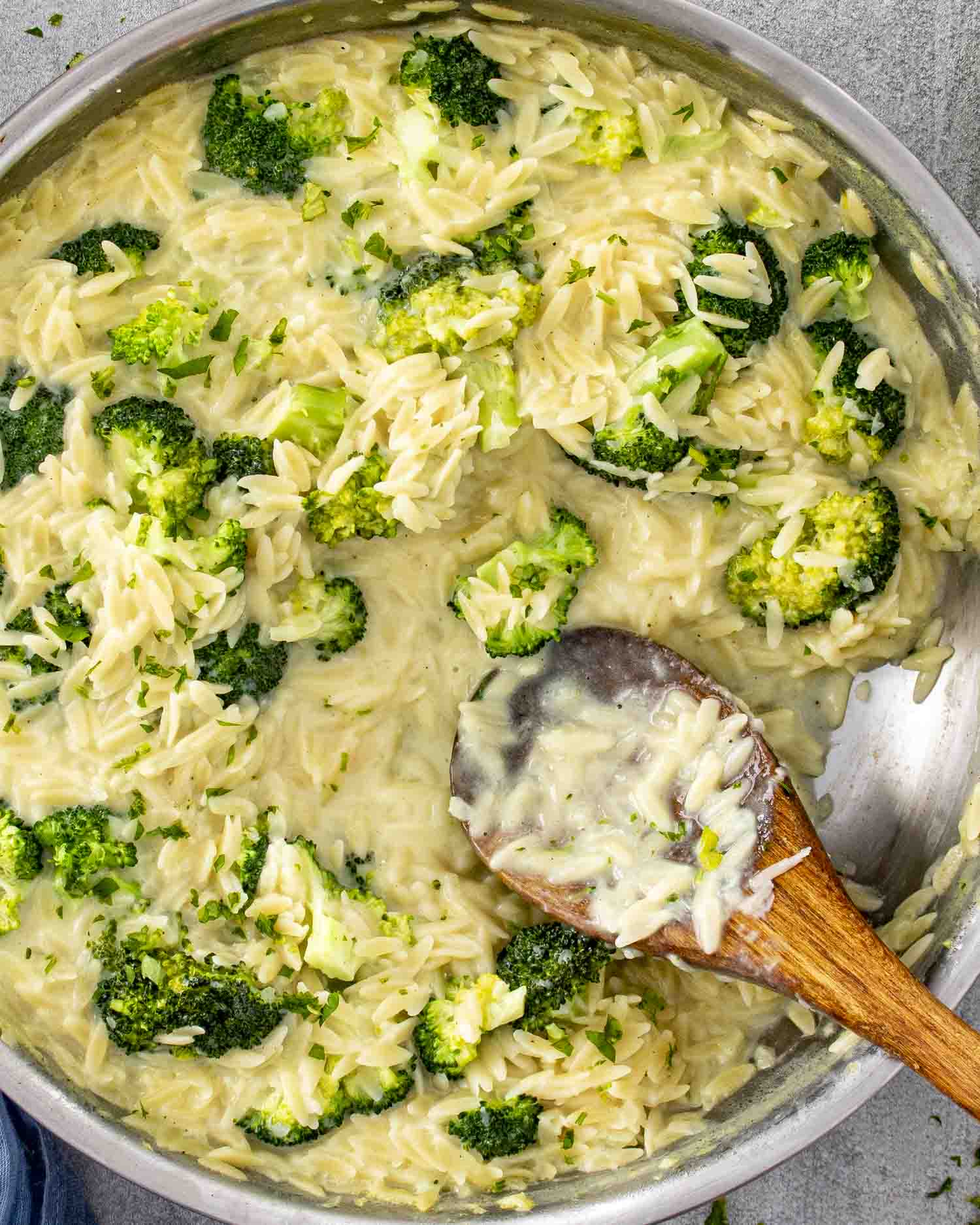 Broccoli cheddar orzo cooking in a skillet with creamy cheese sauce, tender broccoli florets, and orzo stirred together.