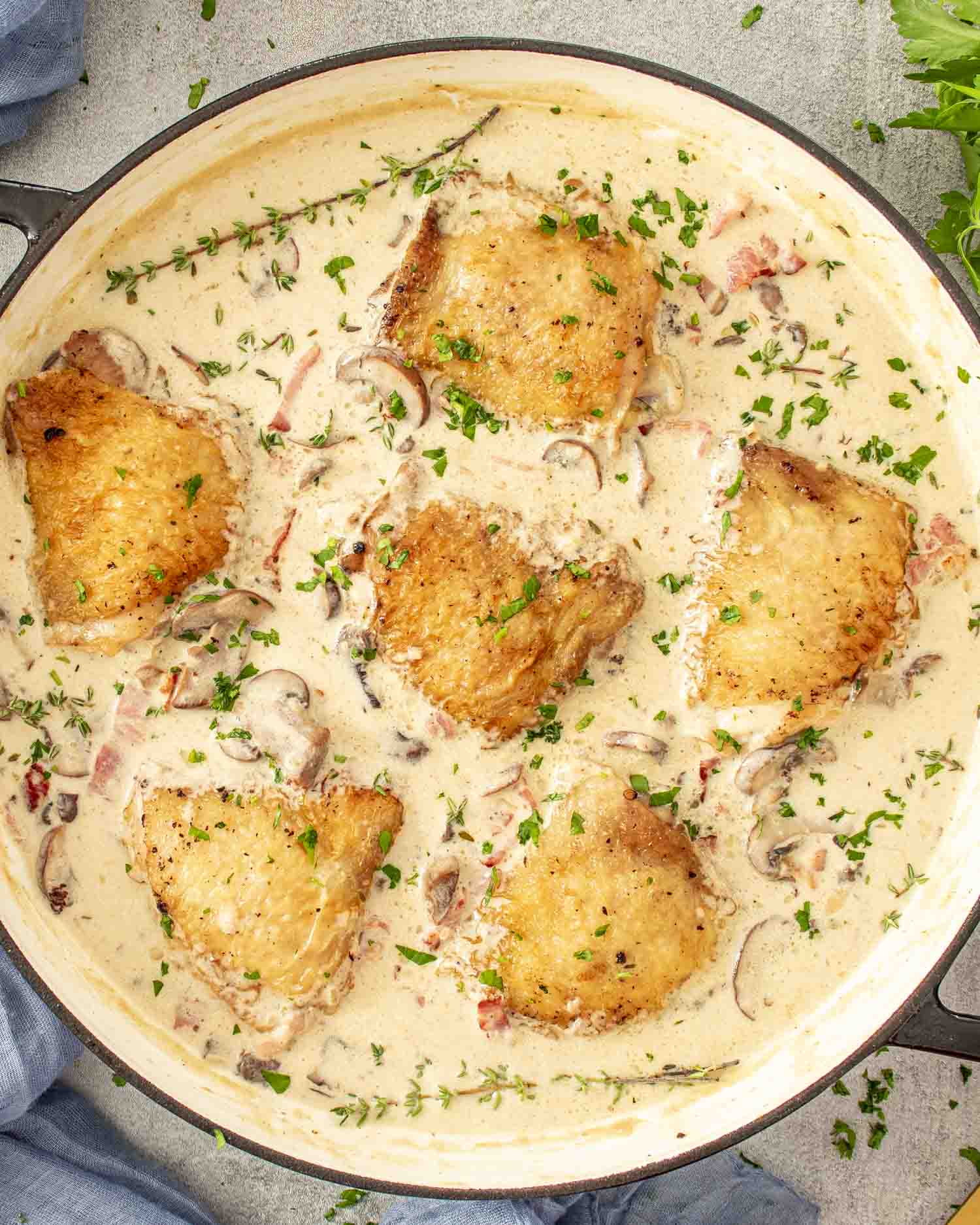 Overhead view of coq au Riesling in skillet with browned chicken thighs, creamy sauce, mushrooms, bacon, and herbs.