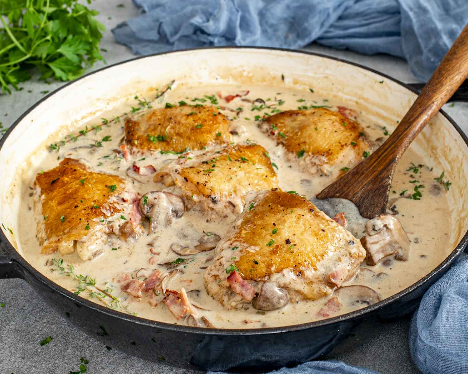 Coq au Riesling simmering in a skillet with golden chicken thighs, mushrooms, bacon, thyme, and creamy white wine sauce.