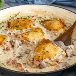 Coq au Riesling simmering in a skillet with golden chicken thighs, mushrooms, bacon, thyme, and creamy white wine sauce.