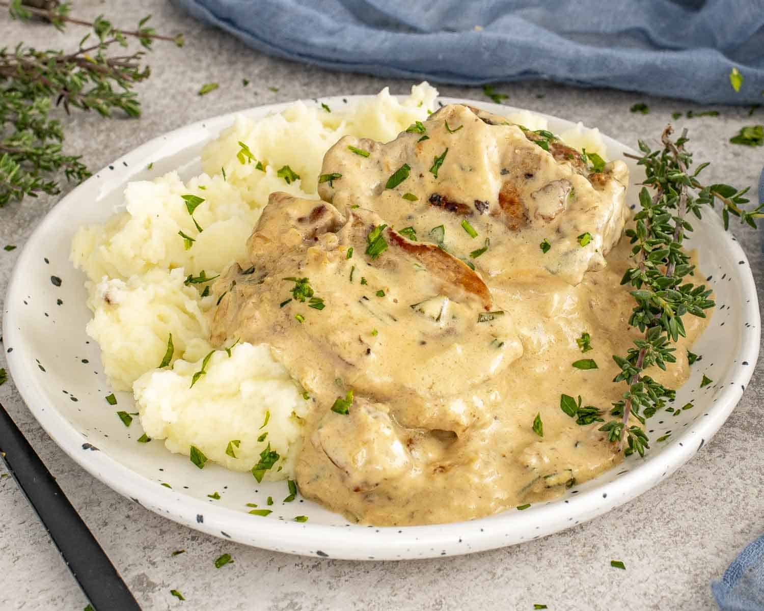 Juicy pork medallions smothered in creamy garlic sauce, served with mashed potatoes and fresh thyme garnish.