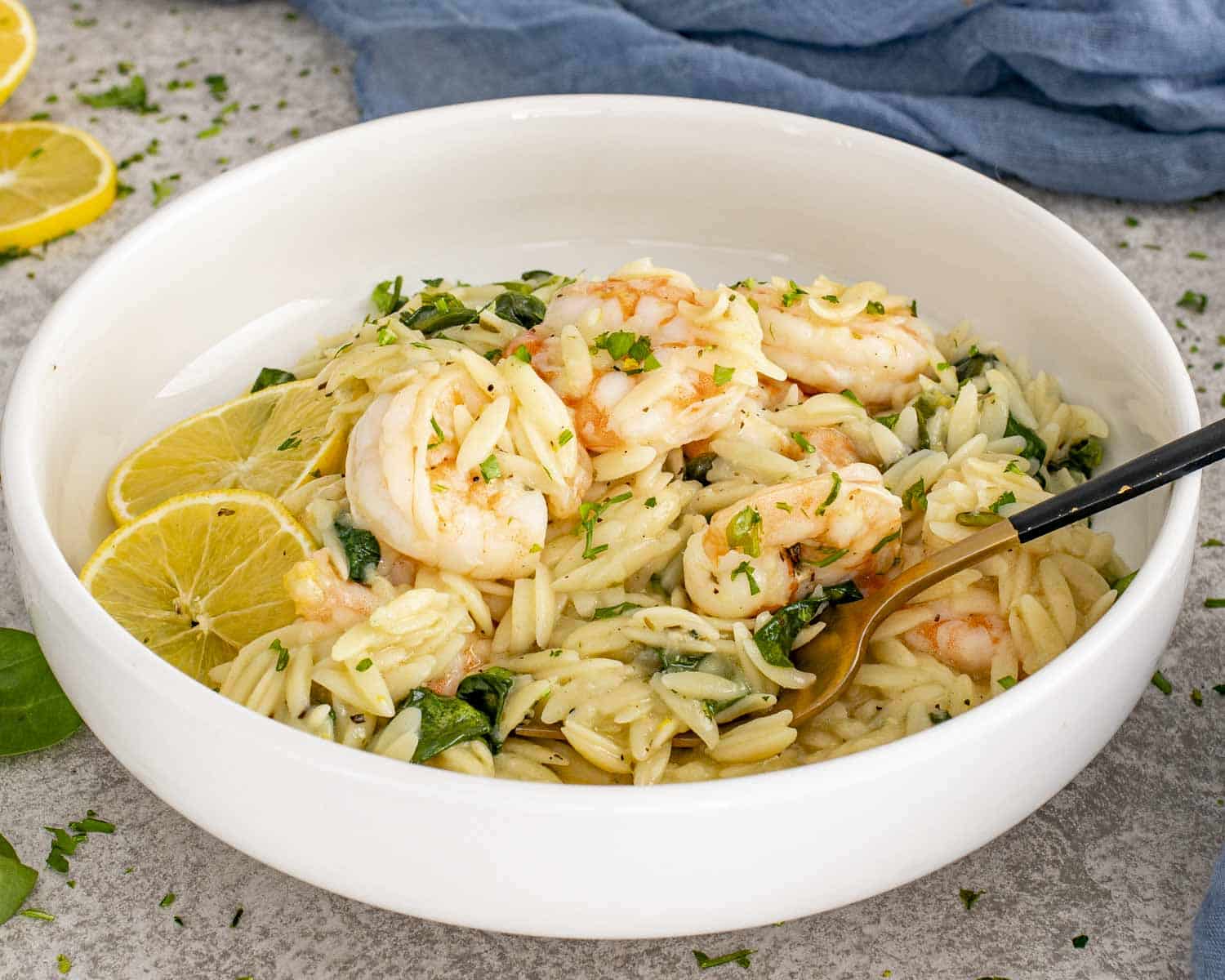 Creamy lemon garlic shrimp orzo served in a white bowl with spinach, Parmesan, and fresh lemon slices.