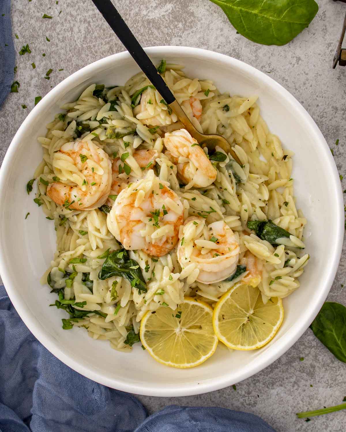 Overhead view of lemon garlic shrimp orzo topped with juicy shrimp, fresh herbs, and lemon slices in a white bowl.