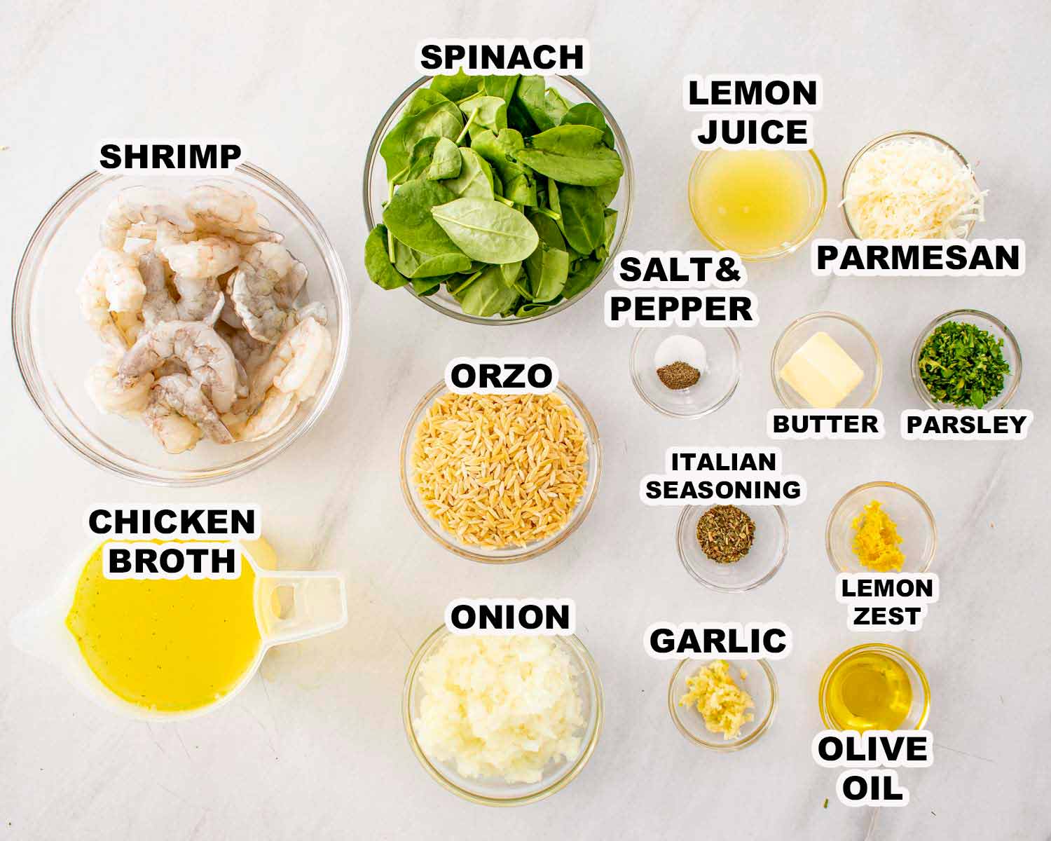 Lemon garlic shrimp orzo ingredients arranged on white surface including shrimp, spinach, orzo, lemon, Parmesan, garlic, and herbs.