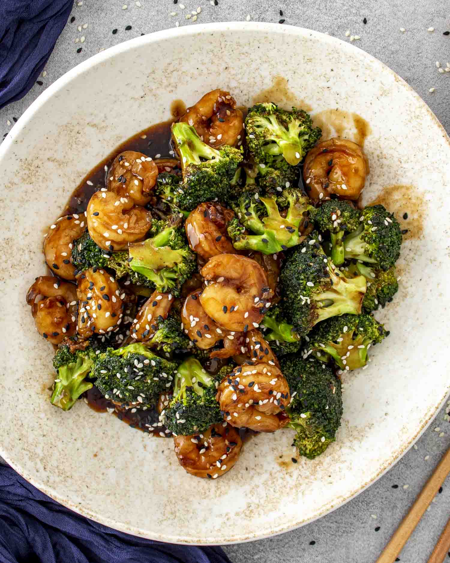 Shrimp and broccoli stir-fry coated in glossy soy garlic sauce, garnished with sesame seeds, served in a shallow bowl.