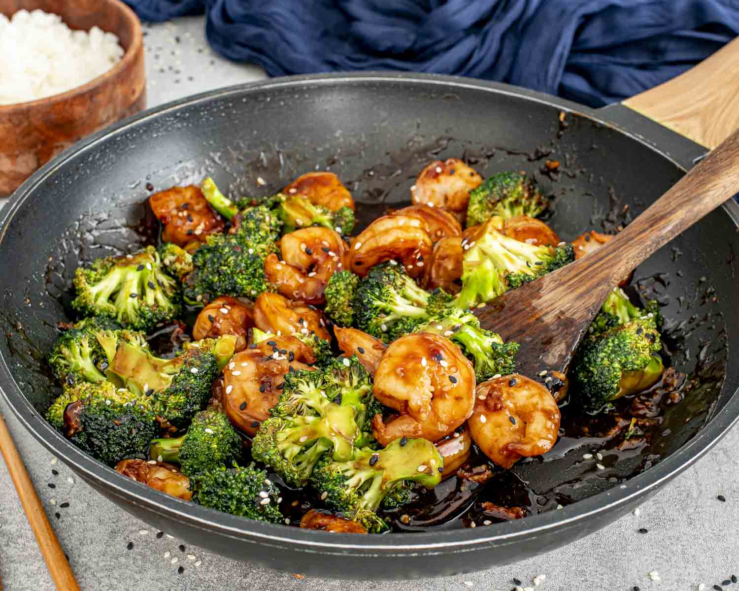 Shrimp and broccoli stir-fry being tossed in a skillet, showing thickened sauce clinging to shrimp and vegetables.