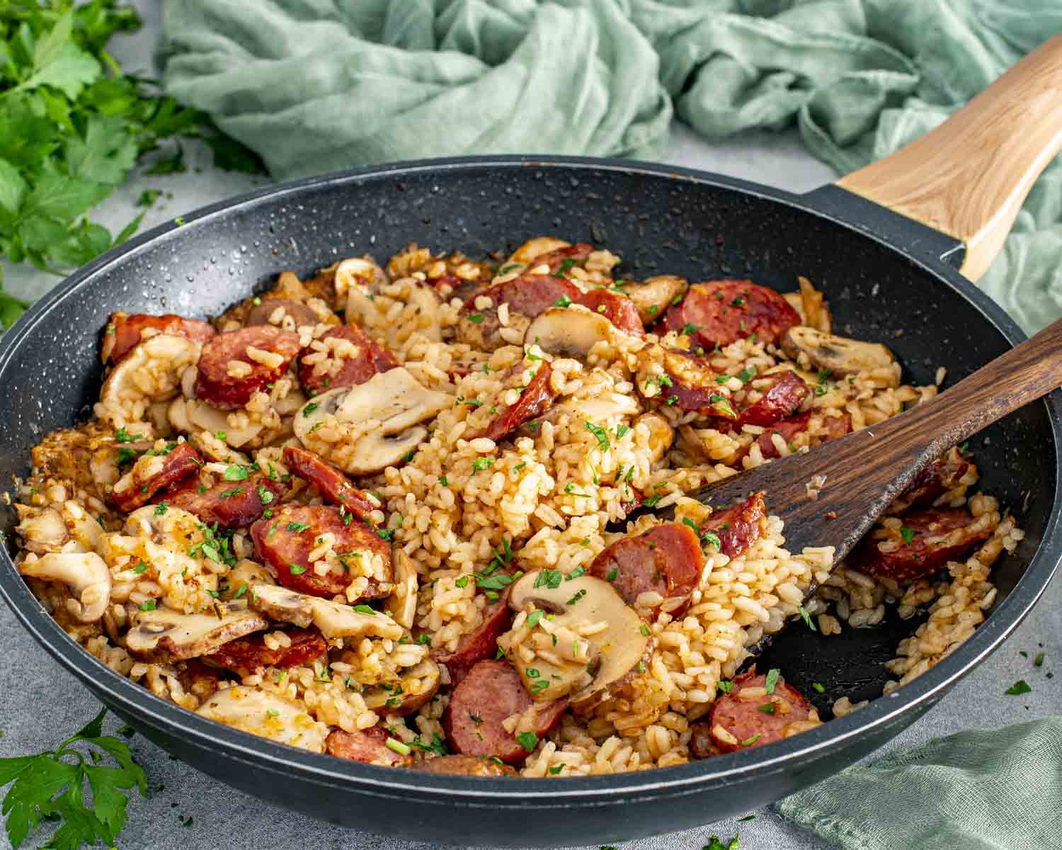 Skillet sausage and mushroom rice being stirred in the pan, showing evenly cooked rice, browned sausage, mushrooms, and herbs.