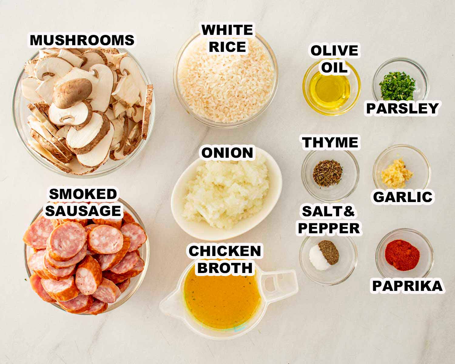 Ingredients for skillet sausage and mushroom rice including smoked sausage, mushrooms, rice, onion, garlic, herbs, and chicken broth.
