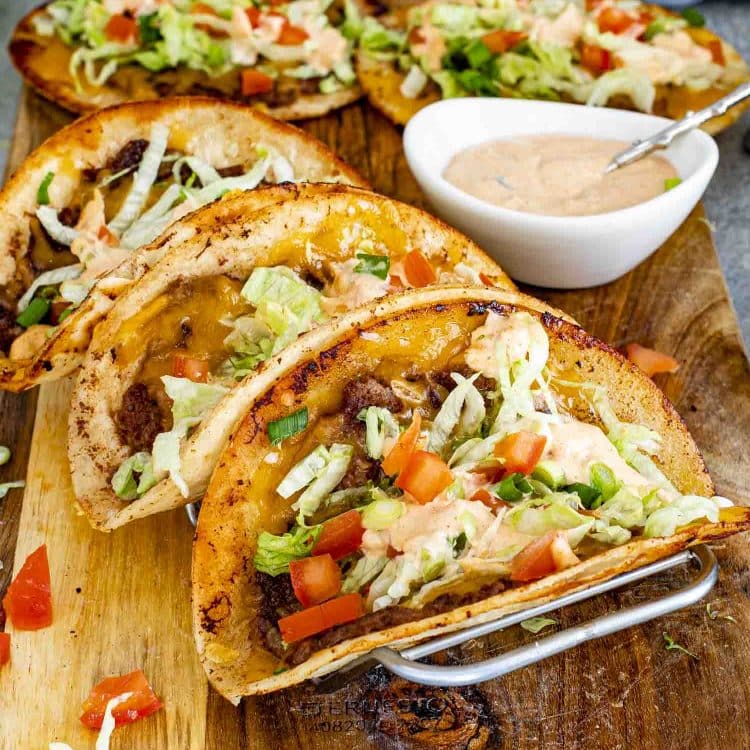 Smashed burger tacos resting in taco holder with crisp tortillas, seasoned beef, melted cheese, and classic toppings.