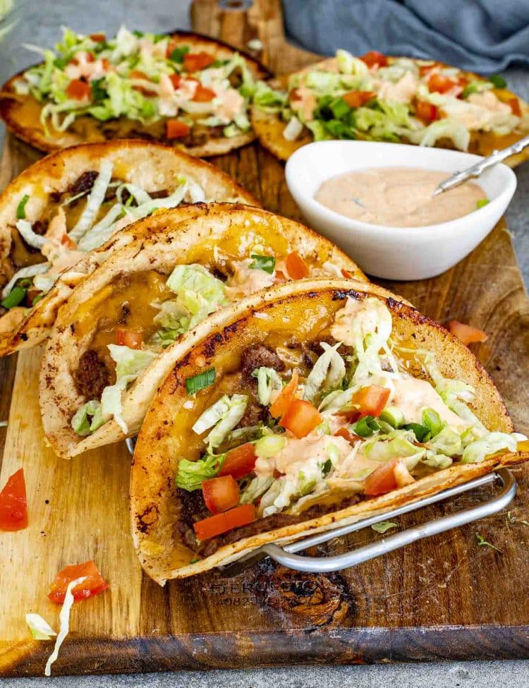 Smashed burger tacos resting in taco holder with crisp tortillas, seasoned beef, melted cheese, and classic toppings.