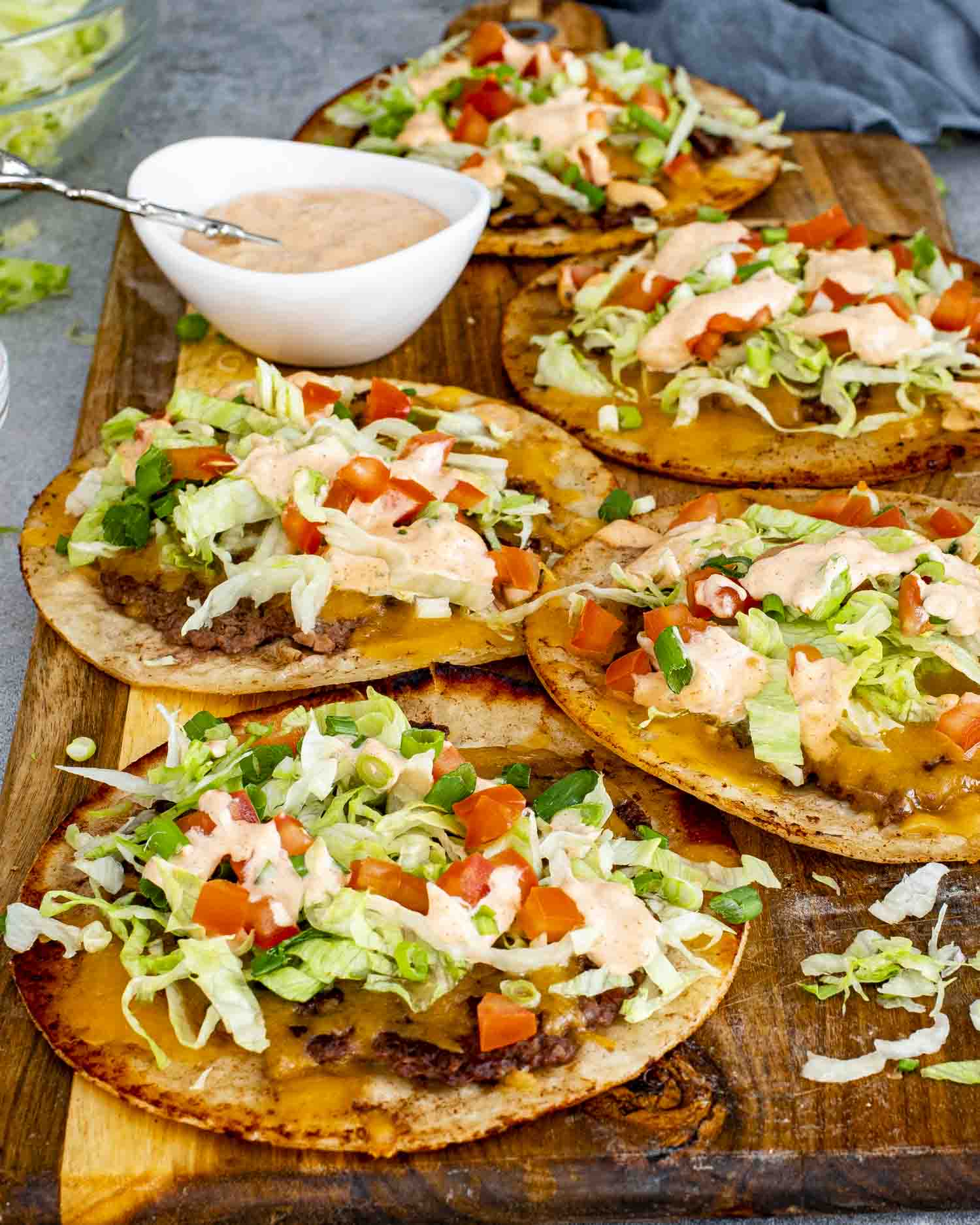 Smashed burger tacos stacked on cutting board with burger sauce, shredded lettuce, diced tomatoes, and green onions.