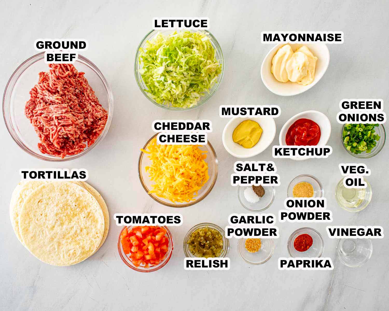 Ingredients for smashed burger tacos including ground beef, tortillas, cheddar cheese, lettuce, tomatoes, Big Mac style sauce components.