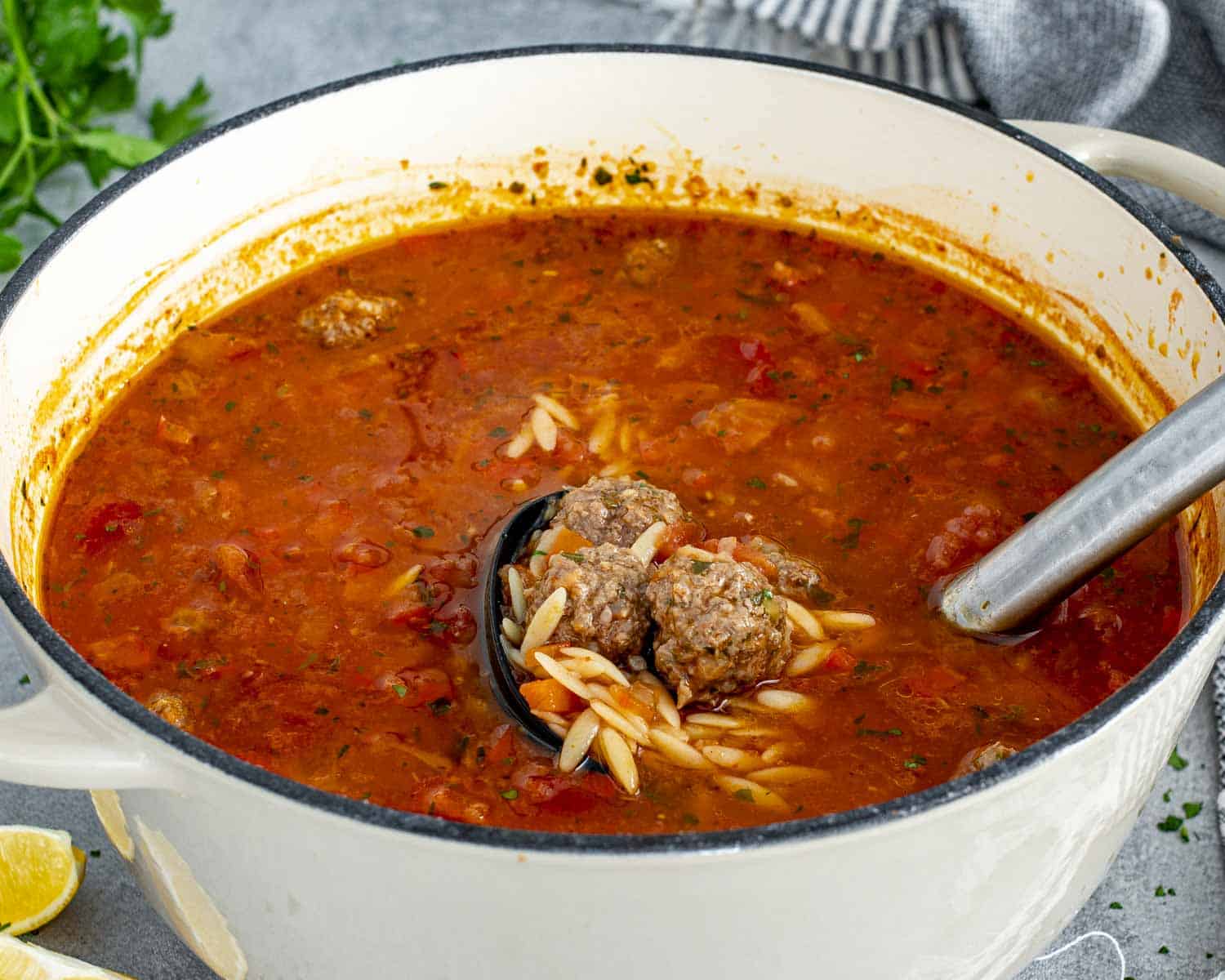 Turkish meatball soup in pot with ladle resting inside, showing hearty tomato broth, orzo, and small beef meatballs.