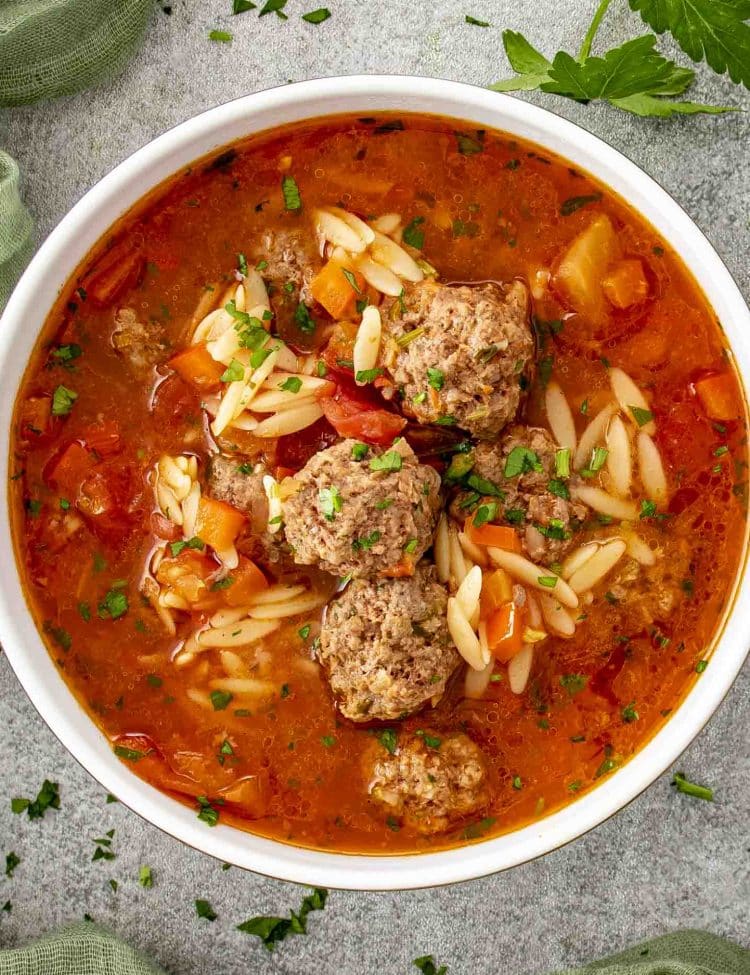 Top view of Turkish meatball soup with small beef meatballs, orzo pasta, diced vegetables, and fresh parsley.