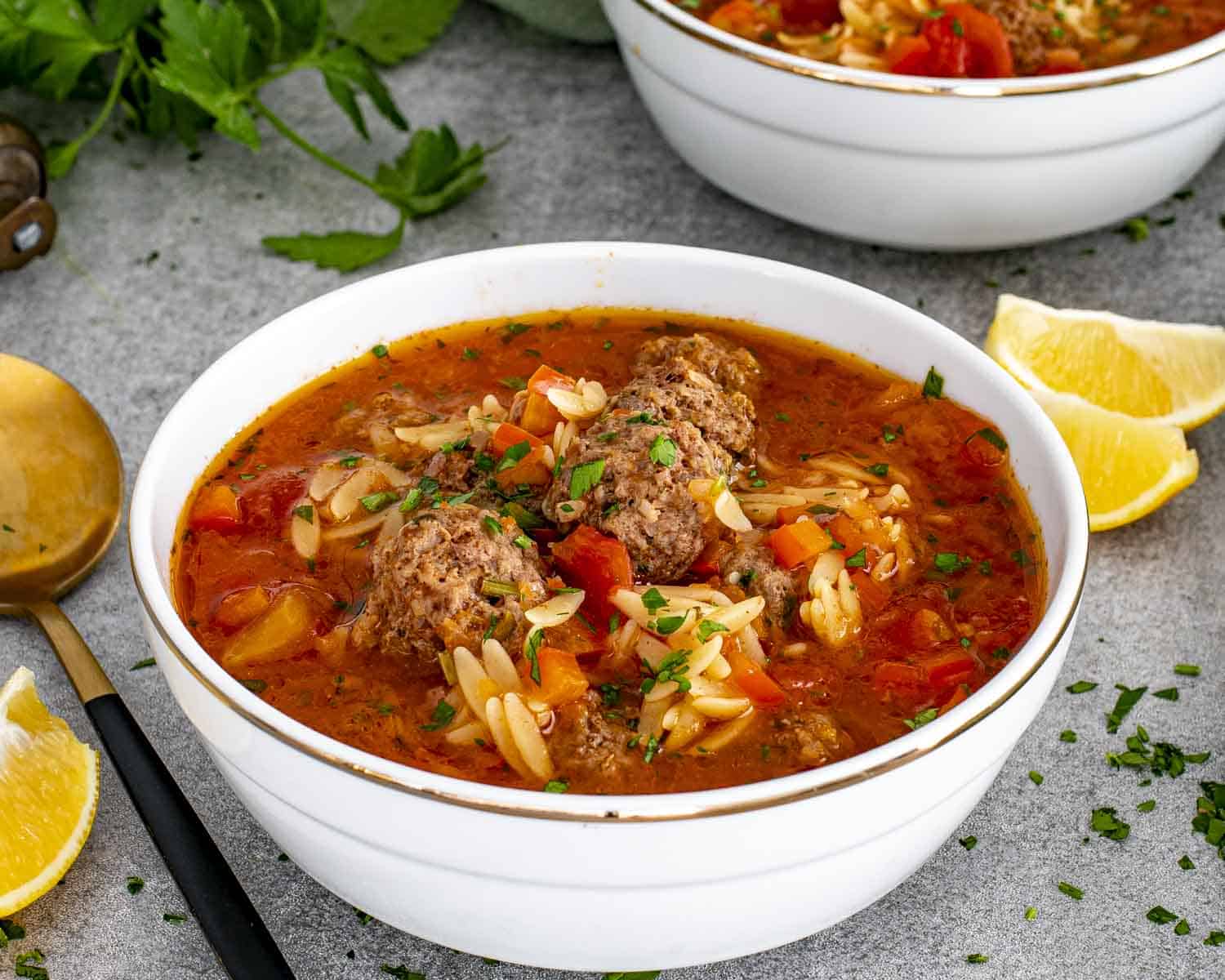 Close-up bowl of Turkish meatball soup highlighting tender meatballs, orzo pasta, vegetables, and vibrant red broth.