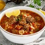 Turkish meatball soup served in white bowl with orzo, beef meatballs, tomato broth, parsley, and lemon on side.