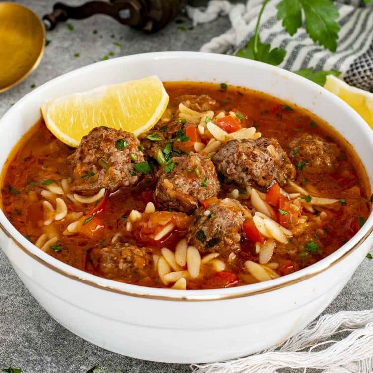 Turkish meatball soup served in white bowl with orzo, beef meatballs, tomato broth, parsley, and lemon on side.