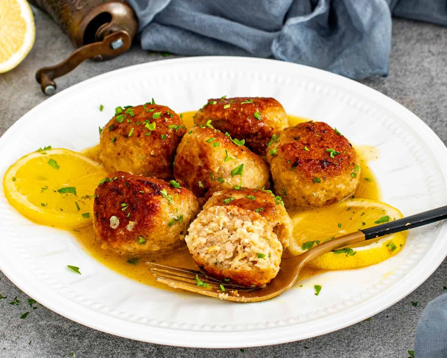 Close up of Chicken Meatballs in Lemon Butter Sauce with one meatball cut open to show the juicy interior.