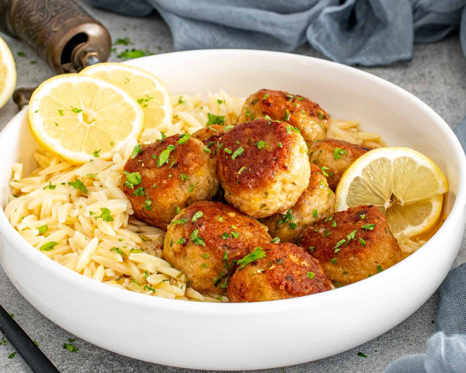 Chicken Meatballs in Lemon Butter Sauce plated with orzo and garnished with lemon slices and chopped parsley.