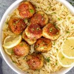 Golden Chicken Meatballs in Lemon Butter Sauce served over orzo pasta with fresh lemon slices and parsley.