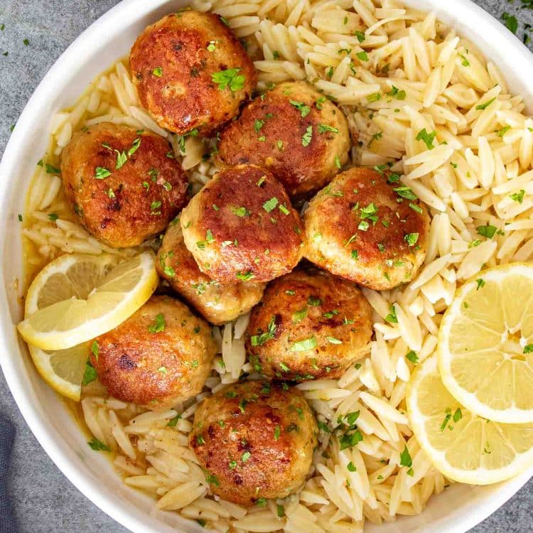 Golden Chicken Meatballs in Lemon Butter Sauce served over orzo pasta with fresh lemon slices and parsley.