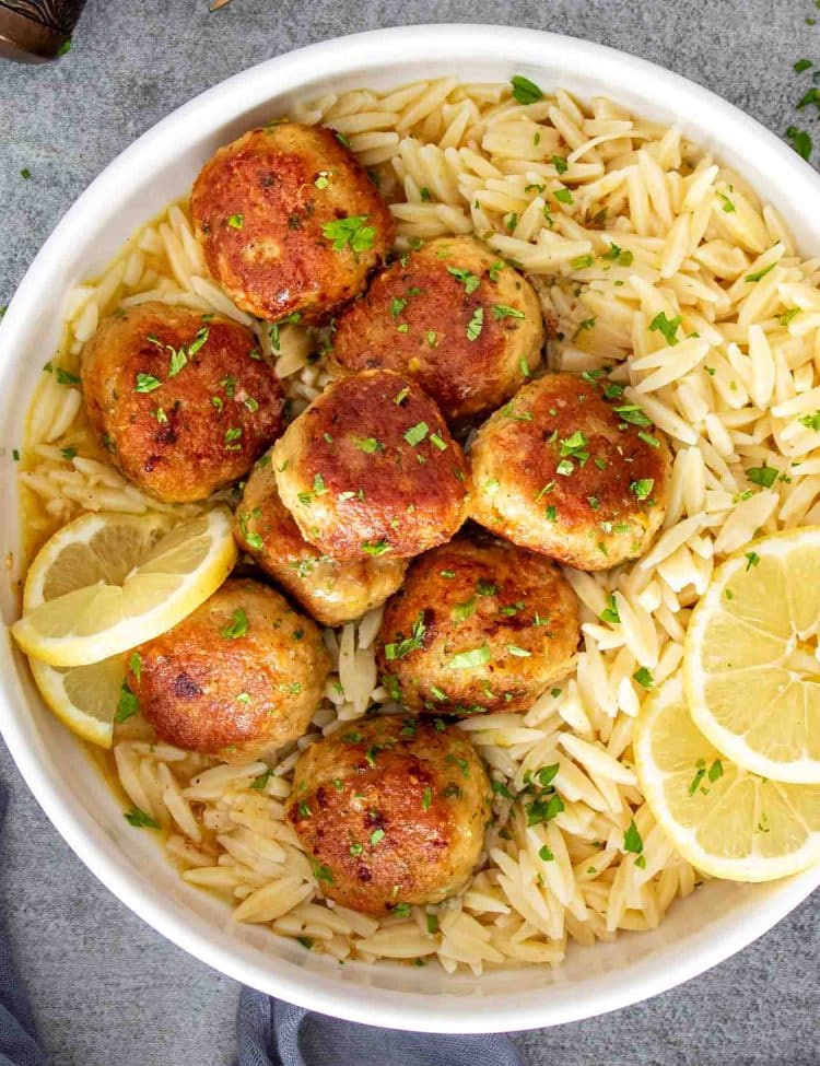 Golden Chicken Meatballs in Lemon Butter Sauce served over orzo pasta with fresh lemon slices and parsley.