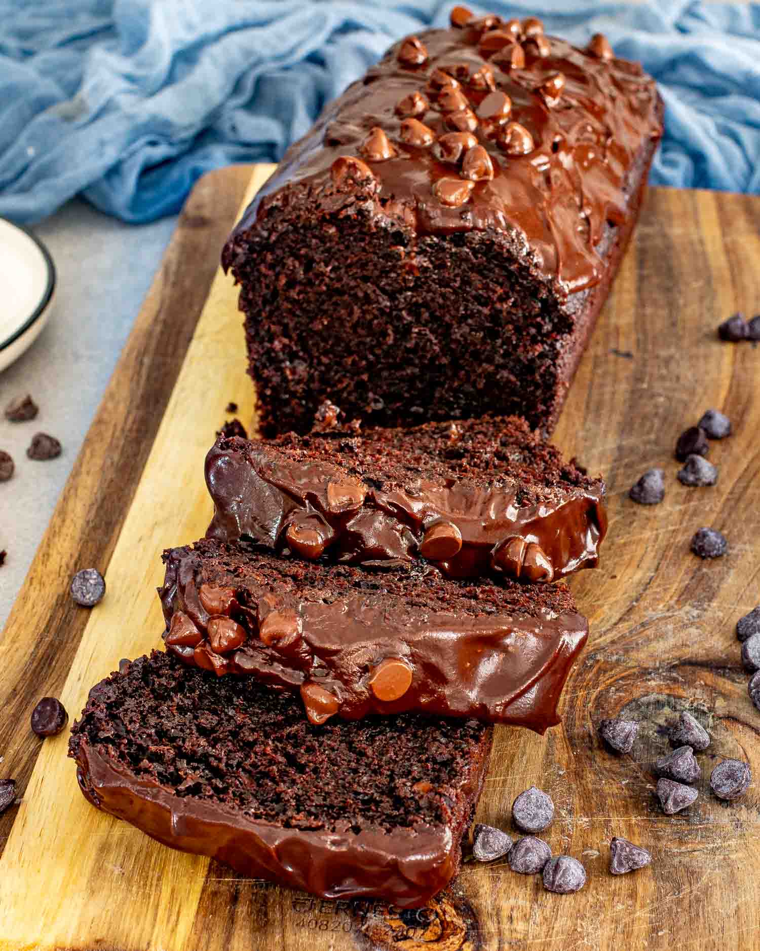 Chocolate loaf cake sliced and served on cutting board with visible chocolate chips and ganache topping.
