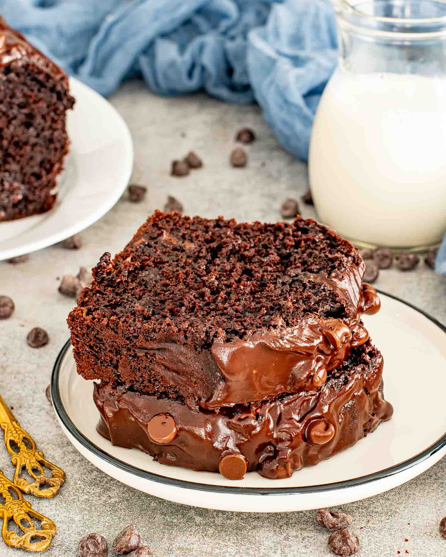 Chocolate loaf cake slice stacked on plate with thick chocolate ganache and scattered chocolate chips.