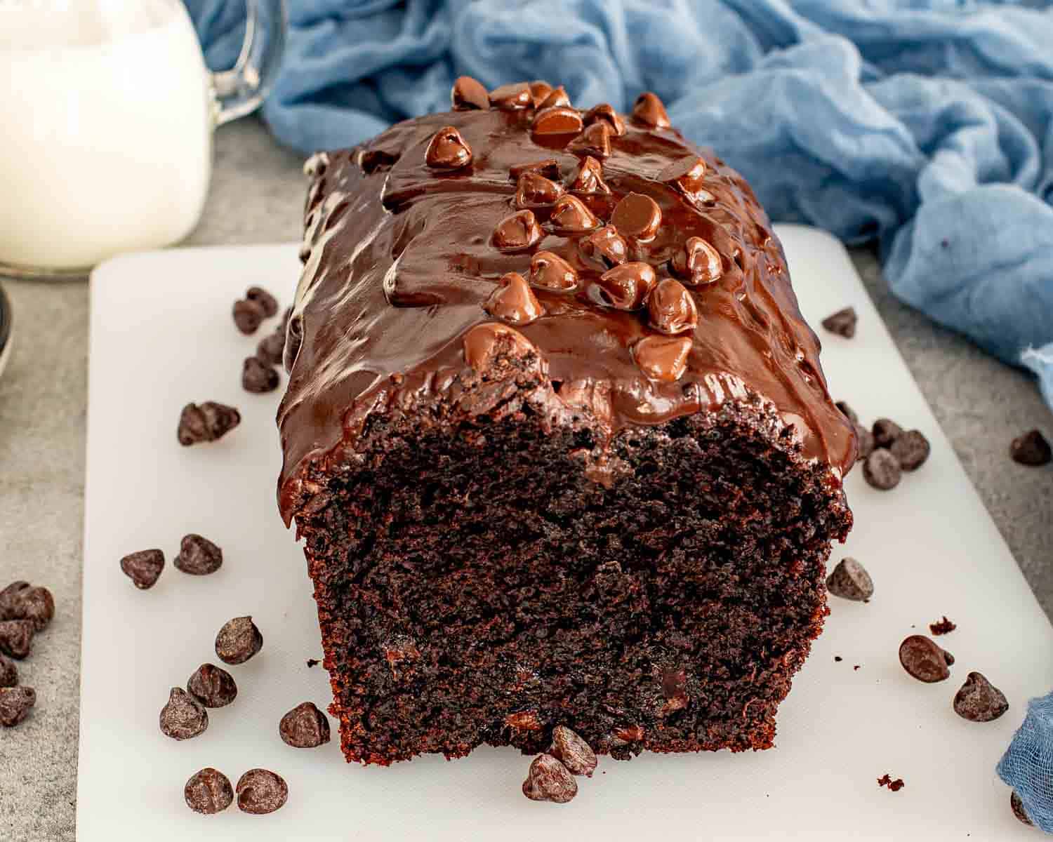 Double Chocolate Loaf Cake loaf covered in glossy chocolate ganache and chocolate chips on a white board.