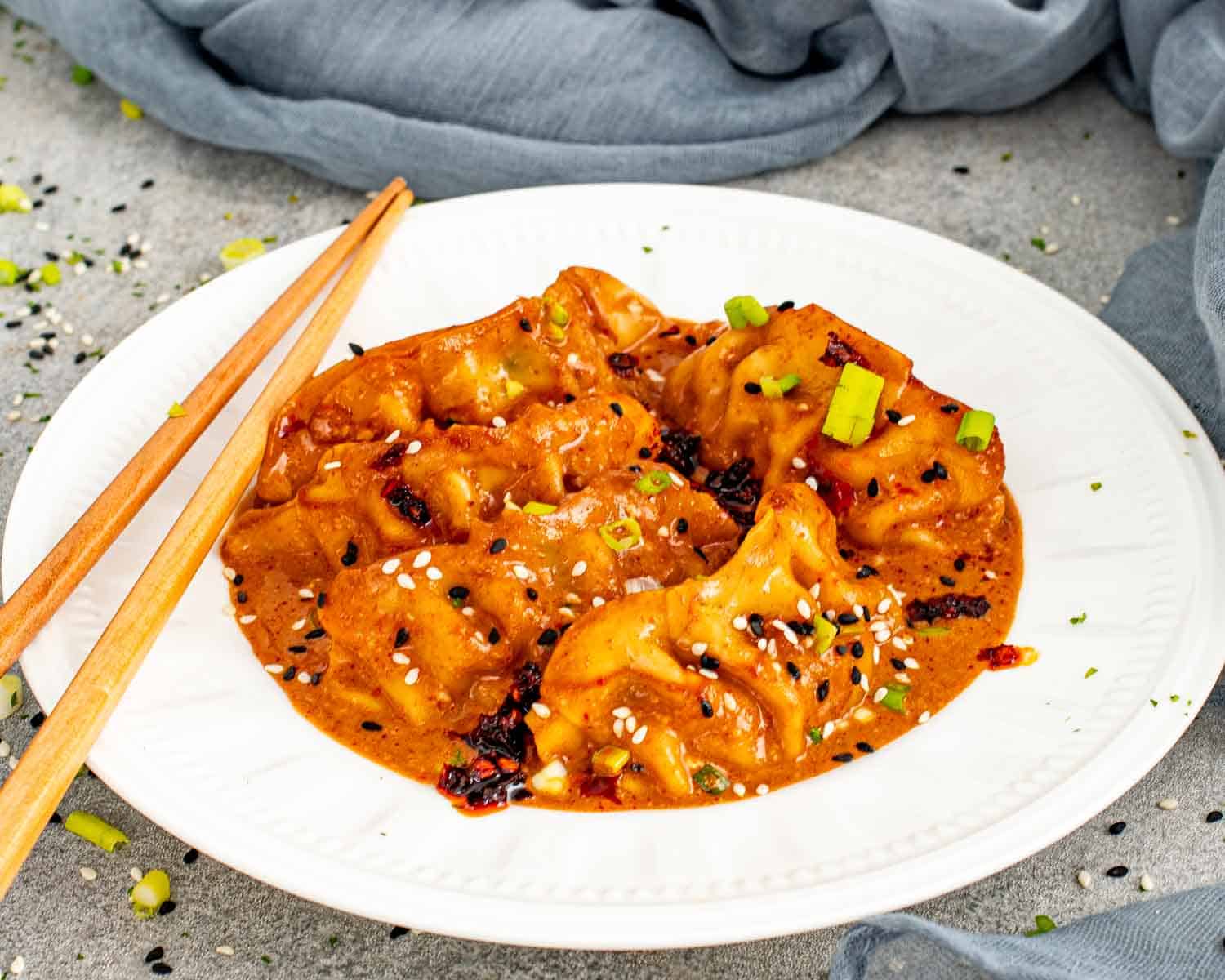 One pan dumplings in creamy red curry sauce with sesame seeds and green onions on white plate.