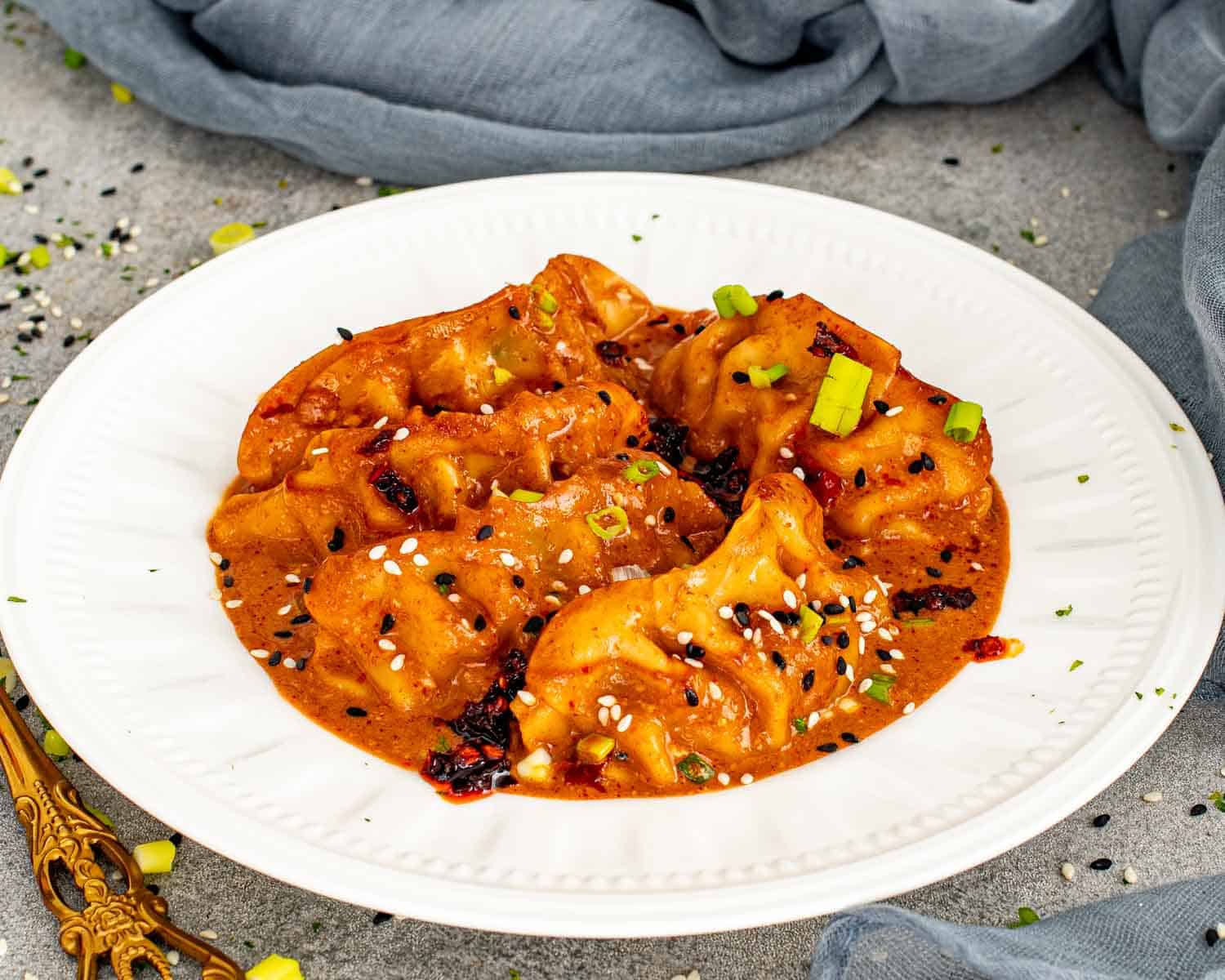 One pan dumplings in creamy red curry sauce with sesame seeds and green onions on white plate.