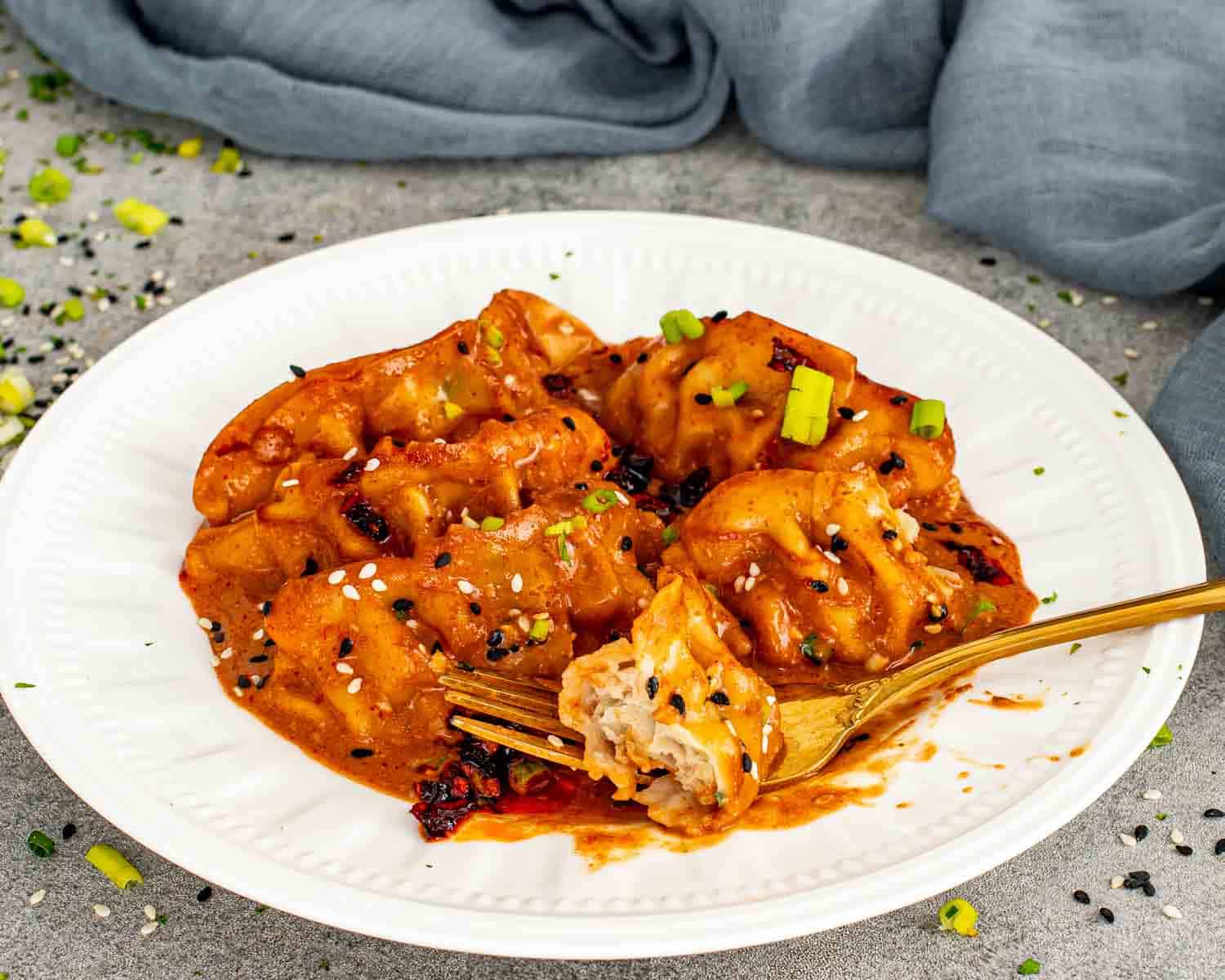 Coconut curry baked dumplings garnished with chili crisp, sesame seeds, and green onions on white plate.