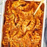 Golden dumplings baked in coconut curry sauce with spoon lifting one from bubbling baking dish.