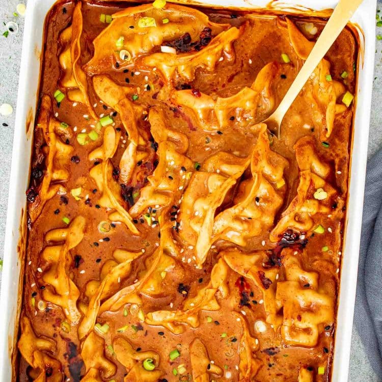 Golden dumplings baked in coconut curry sauce with spoon lifting one from bubbling baking dish.