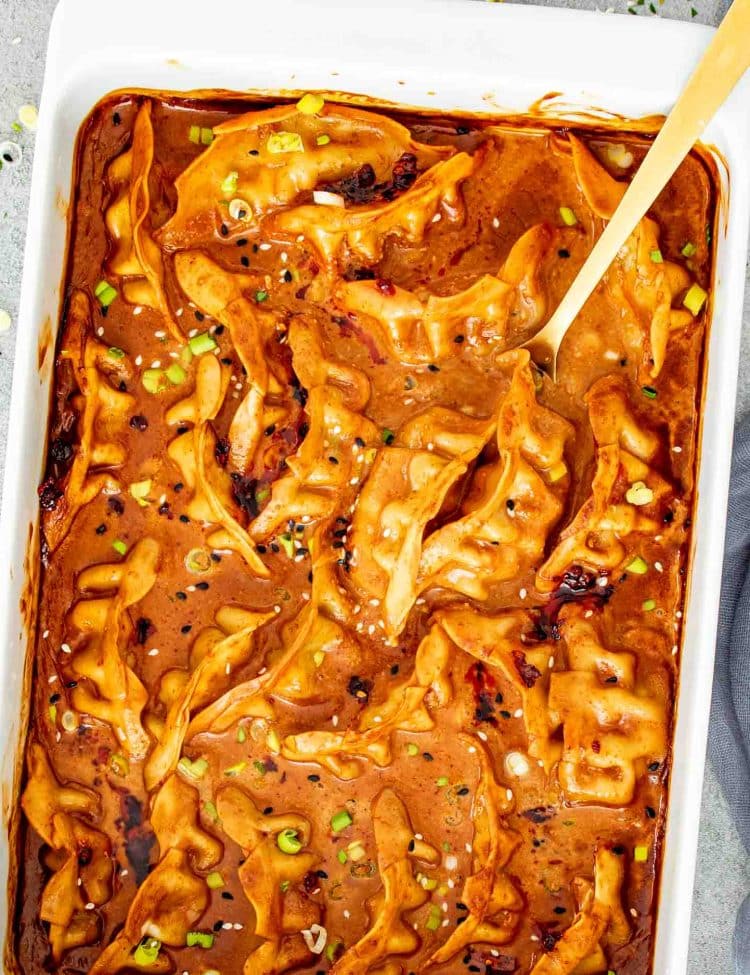 Golden dumplings baked in coconut curry sauce with spoon lifting one from bubbling baking dish.