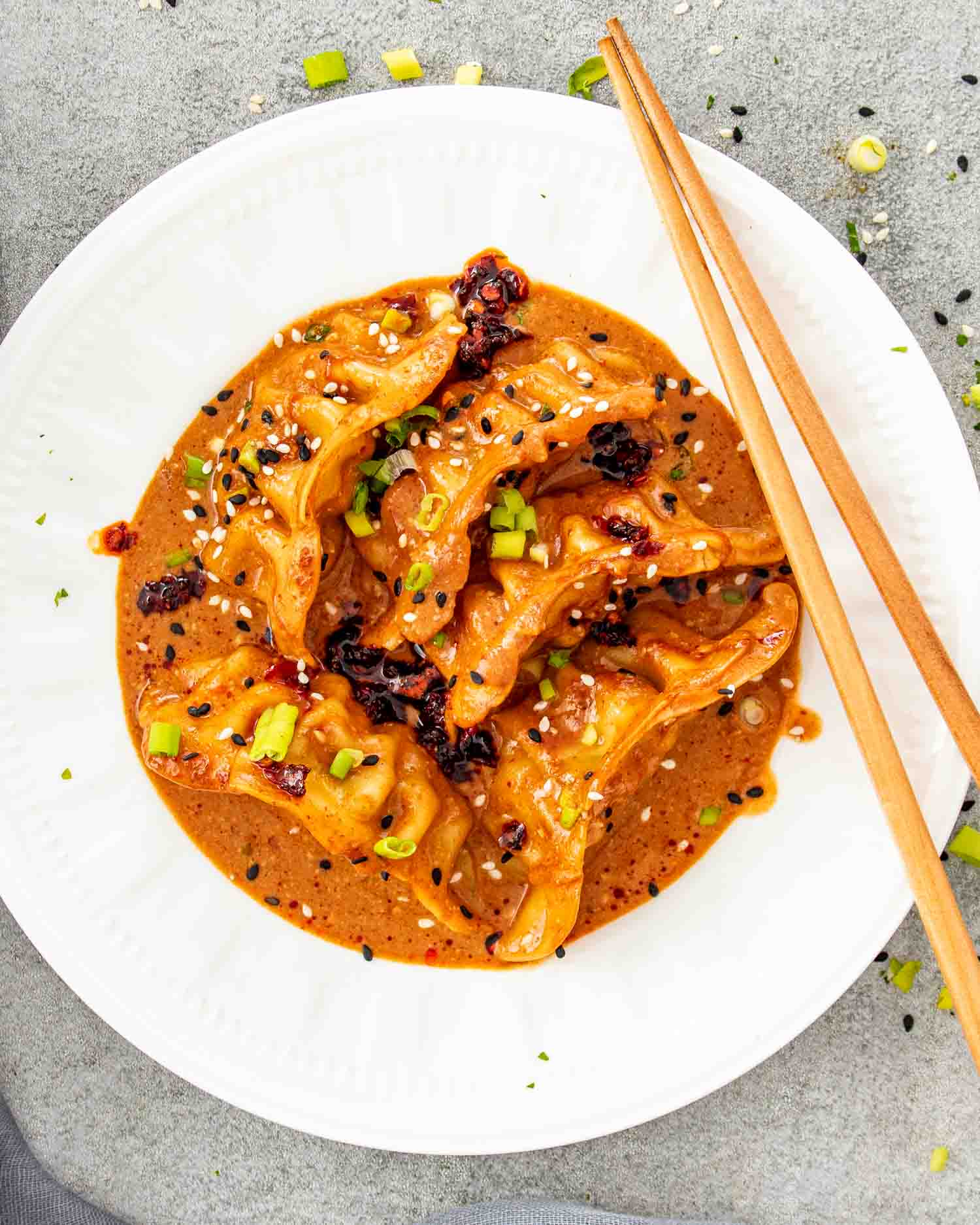 Baked dumplings coated in rich coconut curry sauce served on white plate with chopsticks and chili crisp.