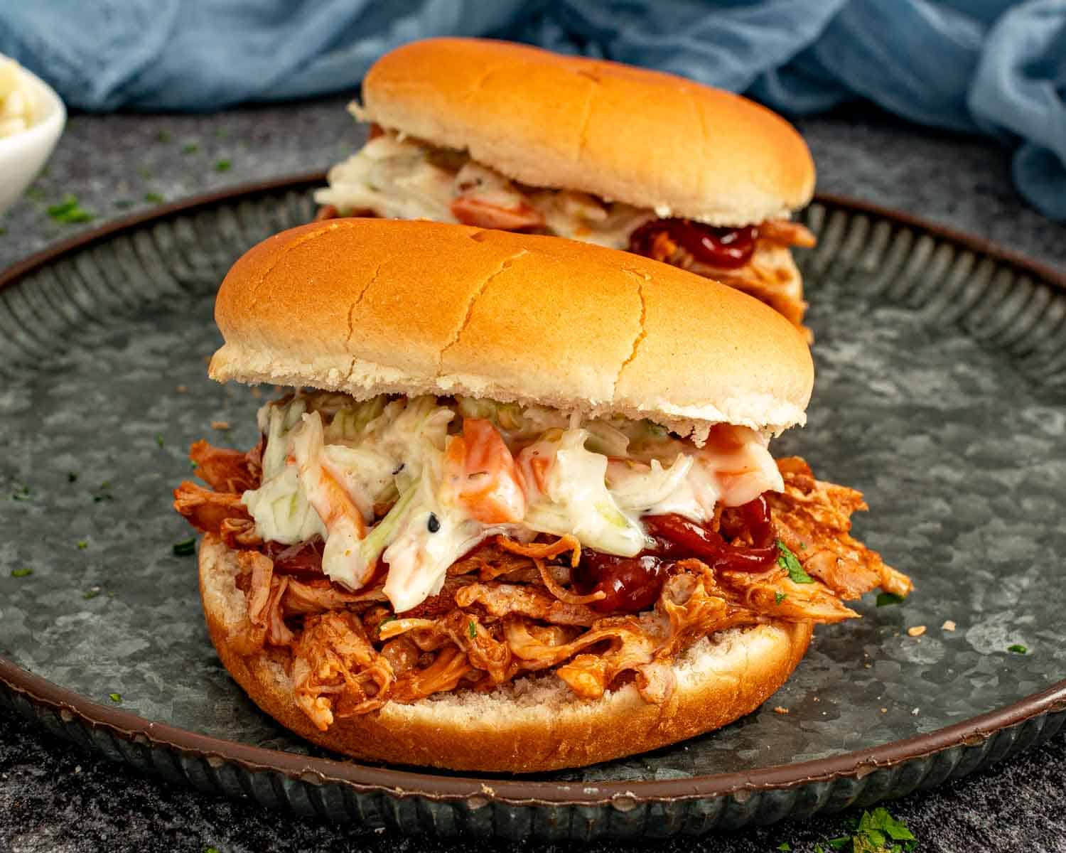 Two slow cooker BBQ pulled pork sliders topped with coleslaw, served on plates for game day or parties.