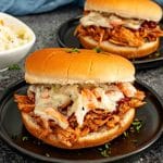 BBQ pulled pork slider topped with creamy coleslaw on a soft bun, served on a dark plate.