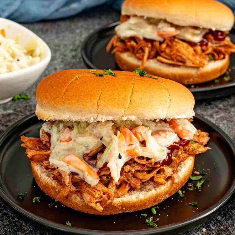 BBQ pulled pork slider topped with creamy coleslaw on a soft bun, served on a dark plate.