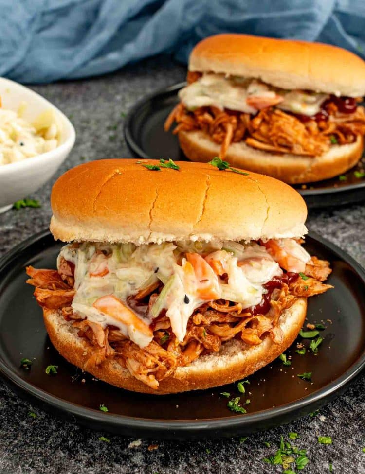 BBQ pulled pork slider topped with creamy coleslaw on a soft bun, served on a dark plate.