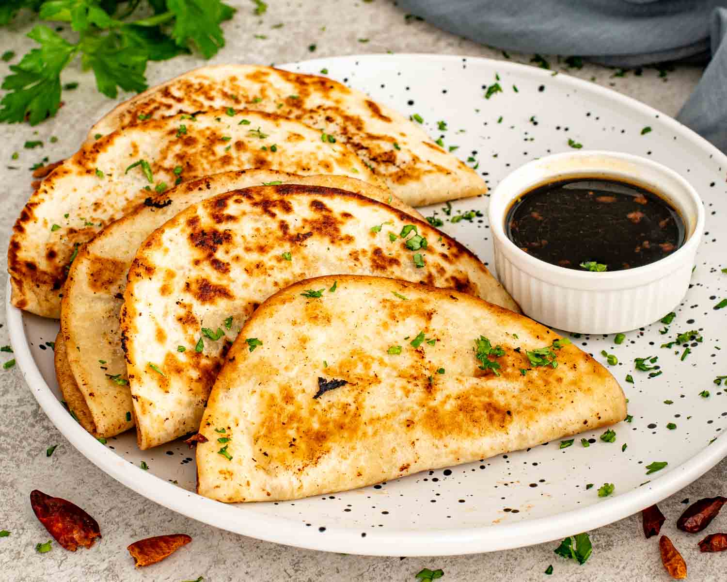 Crispy smashed dumpling tacos arranged on a white plate with soy dipping sauce, garnished with chopped herbs.