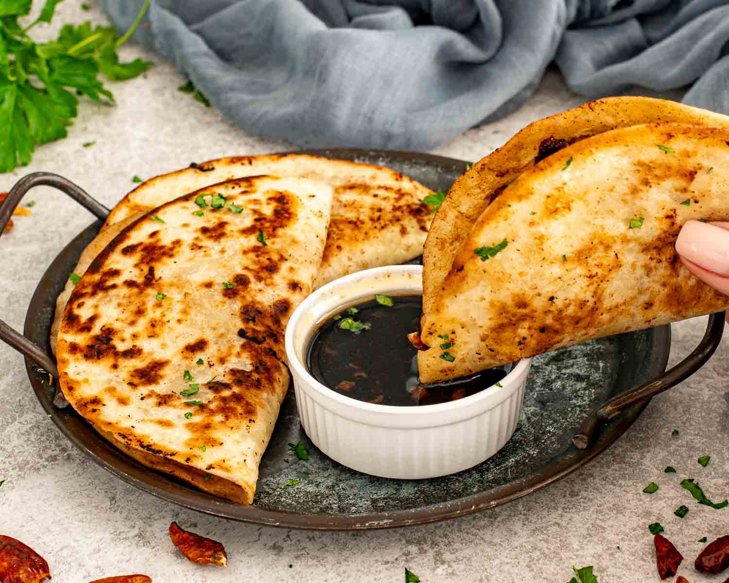 Hand dipping a crispy smashed dumpling taco into soy dipping sauce, showing browned tortilla and juicy pork filling.