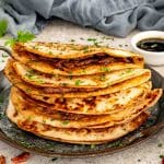 Stack of smashed dumpling tacos cooked until deeply golden and crisp, layered on a skillet with chopped herbs.