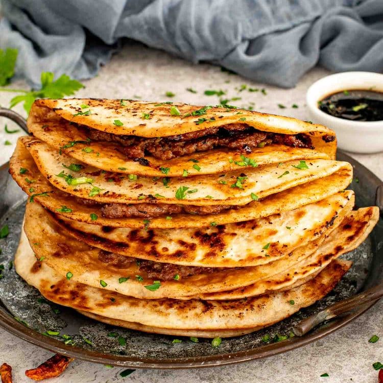 Stack of smashed dumpling tacos cooked until deeply golden and crisp, layered on a skillet with chopped herbs.