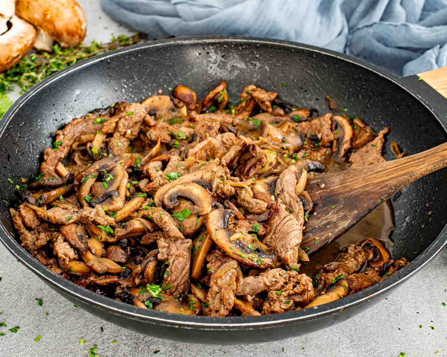 Close up of steak and mushrooms simmering in a skillet with glossy sauce and fresh herbs.