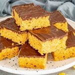 Stack of homemade Butterfinger bars on a white plate with crisp cornflake peanut butter base and chocolate layer.