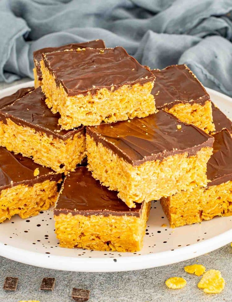 Stack of homemade Butterfinger bars on a white plate with crisp cornflake peanut butter base and chocolate layer.