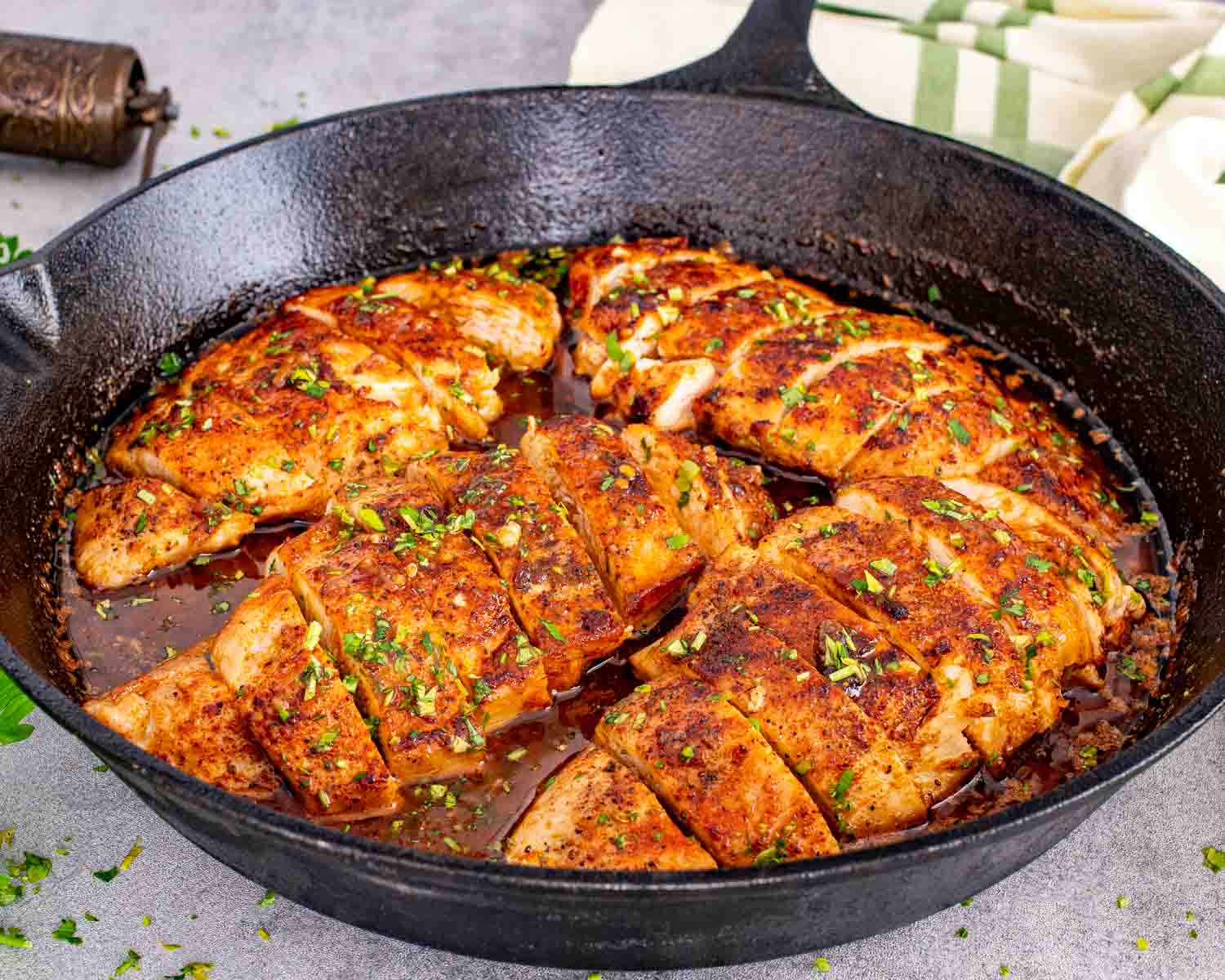 Golden seared chicken breasts in a skillet, coated in a rich, buttery sauce with visible herbs and garlic pieces.