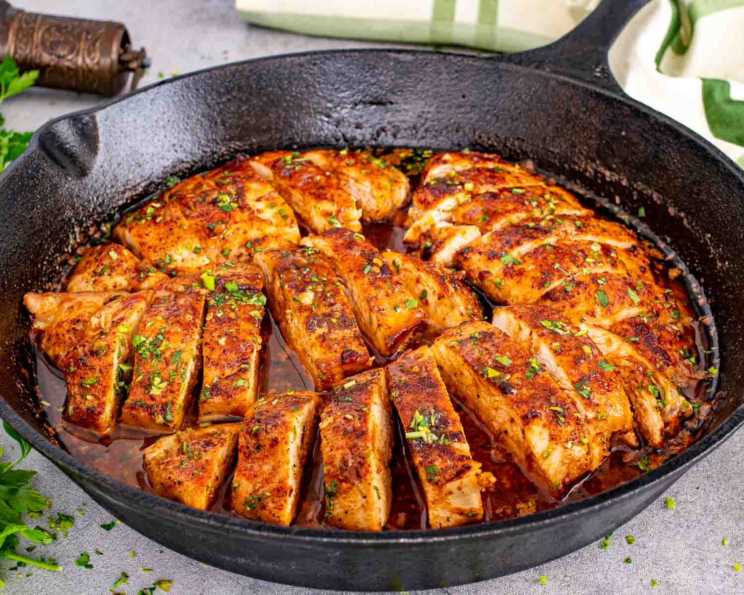 Close-up of juicy chicken breasts simmering in a cast iron skillet with glossy garlic butter sauce and fresh parsley.