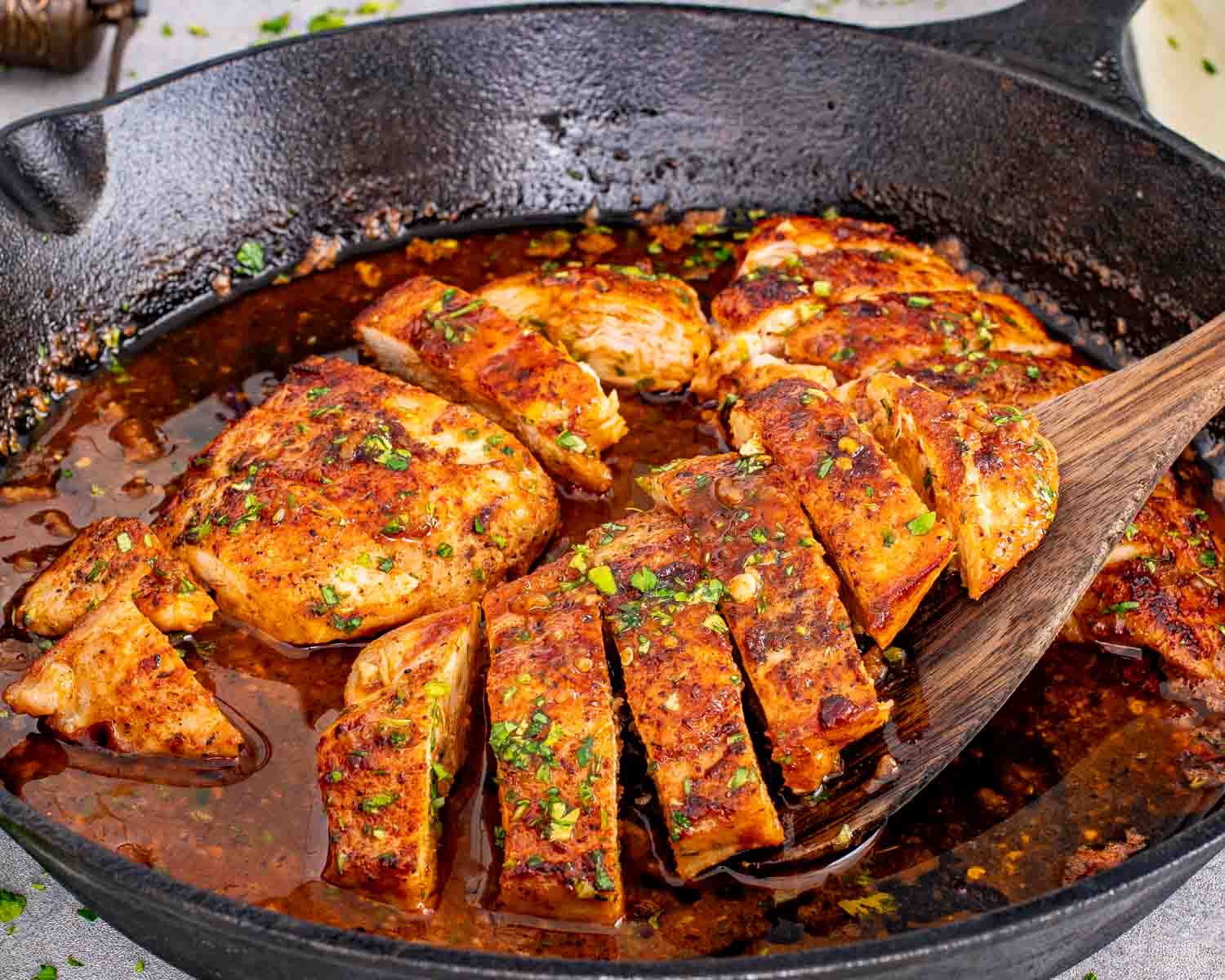 Golden seared chicken breasts in a skillet, coated in a rich, buttery sauce with visible herbs and garlic pieces.